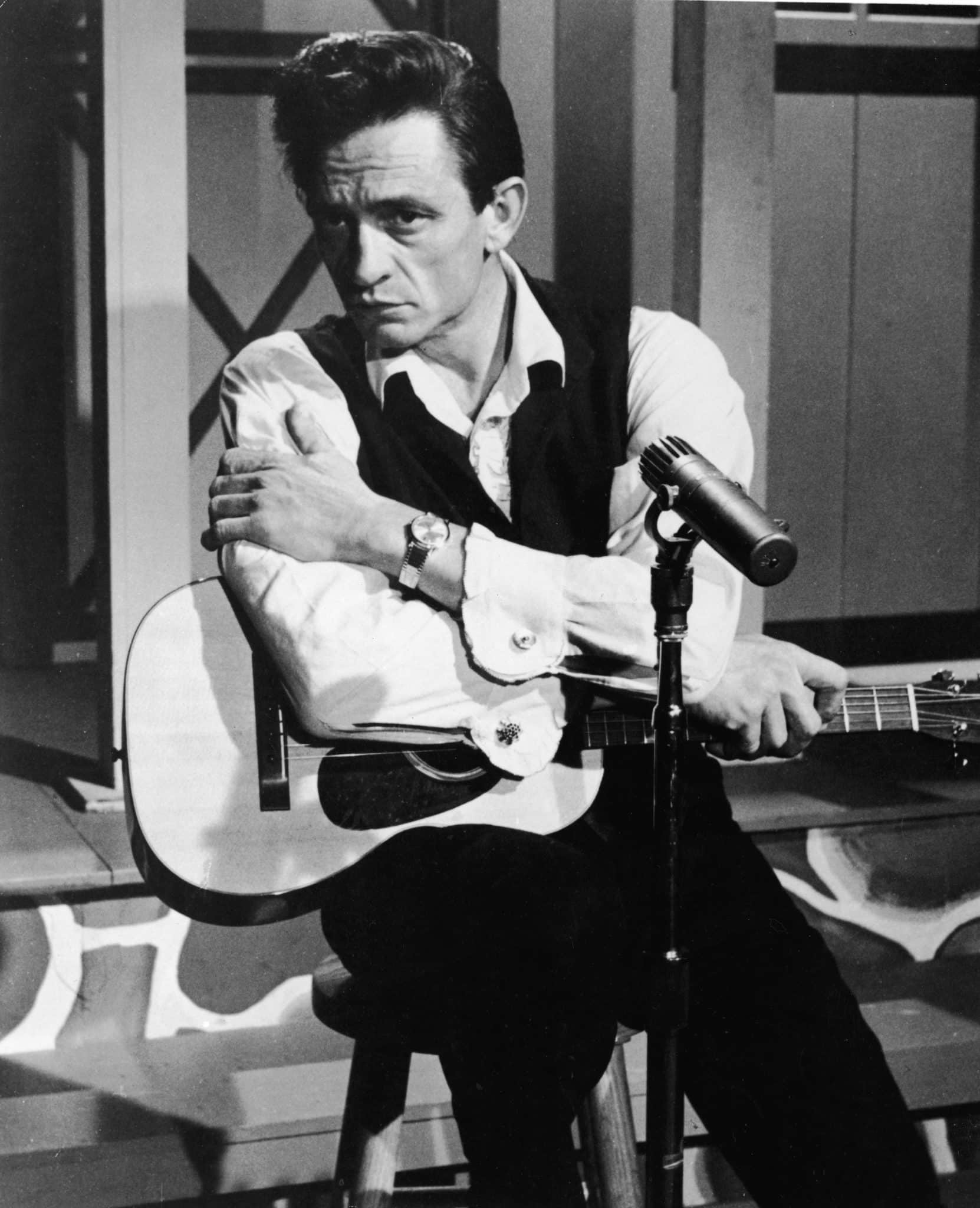 American country singer Johnny Cash (1932 - 2003) sits with an acoustic guitar in a still from the film, 'Road To Nashville,' directed by Will Zenz, 1966. 